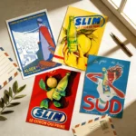 Une vue de dessus de 4 cartes postales d'art vintage de la marque Dzeco Art, disposées sur une surface texturée beige et éclairées par une lumière naturelle. Le pack comprend une illustration d'Alger la Ville Blanche de style affiche de voyage d'époque, et trois publicités rétro pour la marque algéroise Hamoud Boualem, mettant en avant les boissons Slim Le citron qui prime et Sud Boisson Gazéifiée. Deux enveloppes de style courrier aérien rétro et un stylo plume ancien complètent la scène.